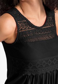 Svart ärmlös topp med intrikata spetsdetaljer på stycket, texturerat mesh i den övre delen och en rynkad kjol.