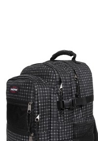 Czarny plecak z siatkowym wzorem, wykonany z trwałej tkaniny. Posiada zamki błyskawiczne, uchwyt oraz siateczkowe kieszenie do przechowywania. Widoczne logo Eastpak.