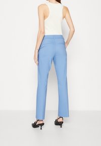 Světle modré kalhoty na míru s rovnými nohavicemi a zadními kapsami, doplněné bílým topem na ramínka a černými lodičkami.