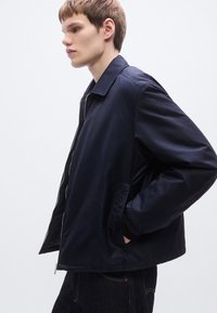 Μπλε ναυτικό μπουφάν με φερμουάρ, διακοσμημένο με υφή, γιακά που ανοίγει πλατιά και ελαστικές μανσέτες. Ο σχεδιασμός διαθέτει άνετη εφαρμογή και πλαϊνές τσέπες.