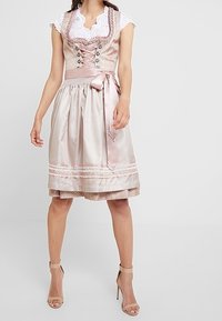 Traditionelle Kleidung mit einem taillierten Mieder aus gemustertem, hellrosa Stoff, weißen Spitzärmeln und einem fließenden, plissierten Rock, der mit einem Satinband gebunden ist.