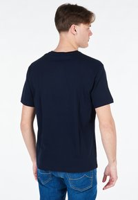 T-shirt di cotone blu navy con maniche corte e colletto a giro, mostrato da dietro. Texture liscia, design semplice, senza ulteriori modelli o dettagli.