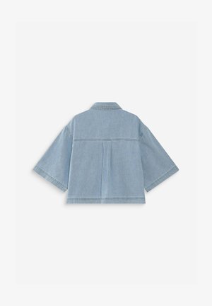 Camisa corta de mezclilla azul claro con mangas anchas de medio largo y un pliegue central en la espalda sobre un fondo blanco liso.