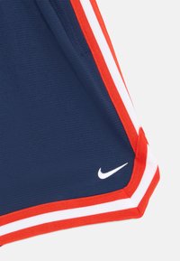 Tumesin sportlühikesed punaste ja valgete külgribadega. Valmistatud tekstuurilisest kangast, mille vasakus alanurgas on väike valge Nike logo.