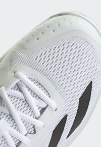 Basket blanc sportif avec une tige en maille respirante, des accents texturés, un col rembourré et des éléments de design noirs distinctifs sur les côtés.