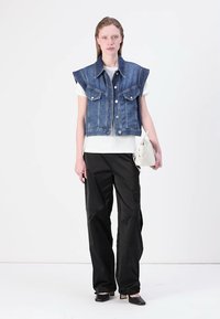 Denim cropped-liivi leveillä kauluksilla, etunapeilla ja kahdella rintataskulla. Päällystetty valkoisella t-paidalla ja yhdistetty löysiin mustiin housuihin ja mustiin kenkiin.