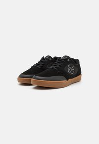Încălțăminte de skate negre cu un superior din suede și textil, talpă din cauciuc de tip gumă, șireturi plate și un accent cu logo pe lateral. Design durabil și cu profil redus.