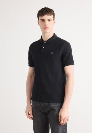 Black polo shirt with a classic collar, two buttons, and an embroidered logo on the left chest. Cotton material; short sleeves, minimal design.