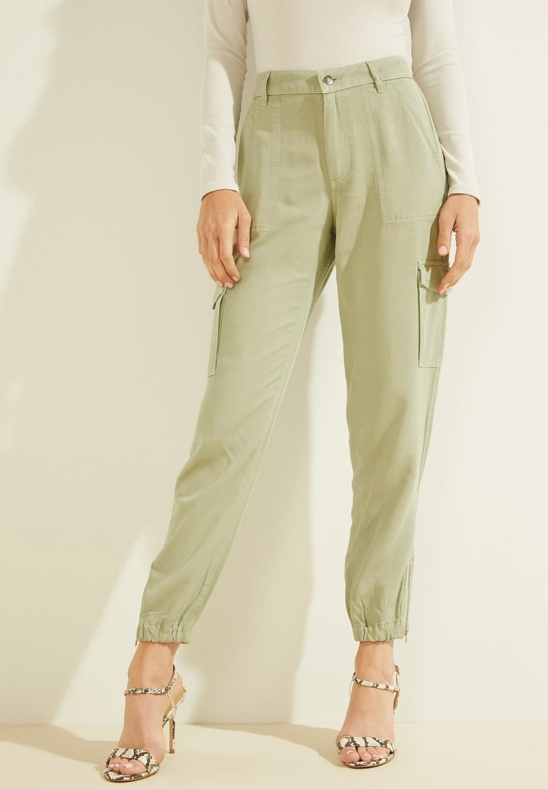 Vaalean oliivinvihreät cargo-housut, joissa on elastiset hihnat, sivutaskut, etupainike ja sileä rakenne. Yhdistetty avonaisiin, remmillä varustettuihin korkokenkiin.