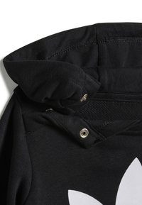 Felpa nera con una trama intrecciata, presenta un cappuccio pieghevole, chiusura a pressione e un grande logo bianco in evidenza sul davanti.