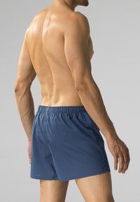 Granatowe kąpielówki wykonane z lekkiego materiału, z elastycznym paskiem w talii, cechujące się luźnym krojem i brakiem widocznych wzorów czy akcentów.