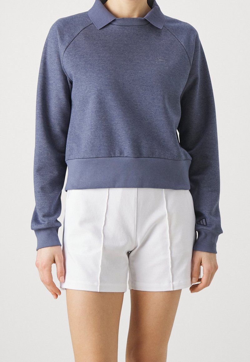 Sudadera azul marino con cuello, puños y dobladillo acanalados. Un par de pantalones cortos blancos debajo, con costuras verticales para un detalle adicional.