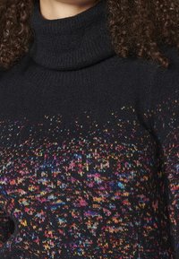 Černý rolák s multicolor vzorem malých, živých teček a texturovaným pletením.