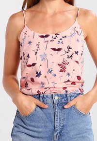 Donna che indossa un top a spaghetto floreale rosa infilato in jeans di denim azzurri a vita alta, con le mani nelle tasche.