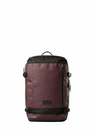 Sac à dos rectangulaire marron foncé avec des accents noirs, poche avant zippée, boucles latérales et poignée supérieure, présenté sur un fond blanc.