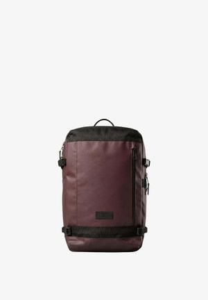 Sac à dos rectangulaire marron foncé avec des accents noirs, poche avant zippée, boucles latérales et poignée supérieure, présenté sur un fond blanc.