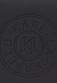 Superficie in pelle nera con un design circolare perforato al centro, caratterizzato dal testo "KARL" e "9 1 M", creando un effetto visivo testurizzato.