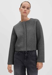 Giacca grigia crop con un motivo texture, collo rotondo e maniche lunghe. Presenta una chiusura frontale ed è abbinata a jeans scuri.