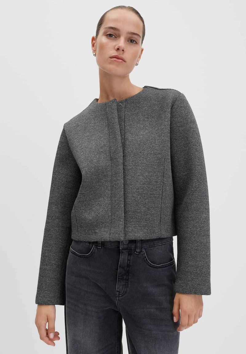 Giacca grigia crop con un motivo texture, collo rotondo e maniche lunghe. Presenta una chiusura frontale ed è abbinata a jeans scuri.