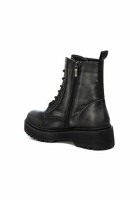 Botín de cuero negro con punta redonda, cremallera lateral, diseño de doble cordones y suela gruesa y texturizada para una mejor sujeción.