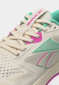 Κοντινή λήψη μπεζ αθλητικού παπουτσιού Reebok με τόνους τιρκουάζ και ροζ, που δείχνει τα κορδόνια, το δίχτυ και το λογότυπο στη γλώσσα και την πλευρά.