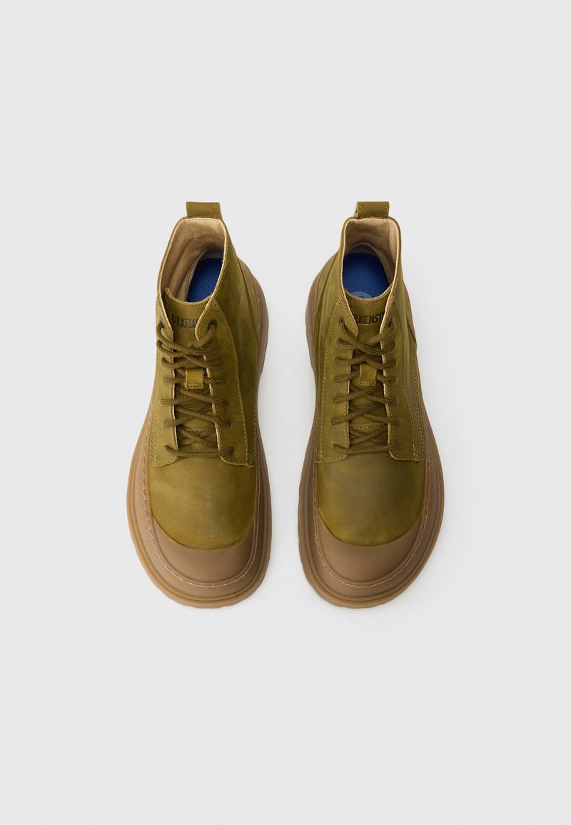 Botas de tobillo de cuero verde con puntera redonda, cierre de cordones en la parte delantera, suela de goma marrón y plantilla azul, con una textura suave y costuras mínimas.