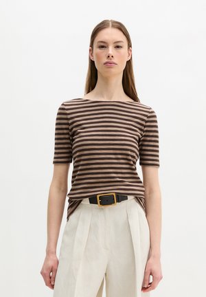 Kobieta ubrana w brązowo-beżową, paskowaną bluzkę z krótkim rękawem, kremowe, plisowane spodnie z wysokim stanem oraz czarny pasek z dużą prostokątną klamrą.