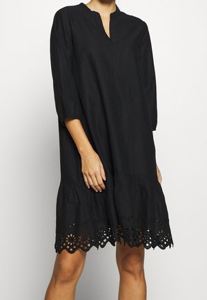 Schwarzes knieumspielendes Kleid mit einem gespaltenen Ausschnitt, dreiviertel Ärmeln und einem dekorativen floralen Cut-out-Muster am Saum. Weiche Stoffstruktur.