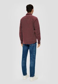 Czerwona i biała w kratkę koszula z długim rękawem, z zapiętymi mankietami, połączona z niebieskimi dżinsami i białymi trampkami, widok z tyłu.