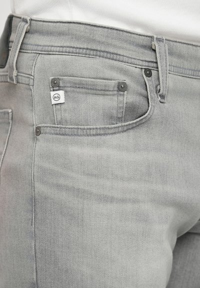 Šedé džíny z denimu s klasickým pětimístným designem, kovovými knoflíkovými detaily a malou značkovou etiketou na zadní kapse.
