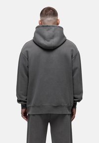 Felpa grigia con cappuccio, dal taglio rilassato, in tessuto spesso e con polsini a coste. Ha un cappuccio spazioso e una texture morbida.