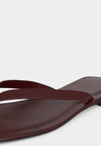 Καφέ δερμάτινο επίπεδο σανδάλι με λεπτά λουράκια και τετράγωνη μύτη, παρουσιασμένο σε απλό φωτεινό φόντο.