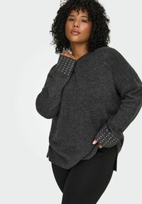 Pletena dukserica u tamnosivoj boji sa V-izrezom, teksturiranim materijalom i dugim rukavima koji imaju srebrne šiljke na manžetama.