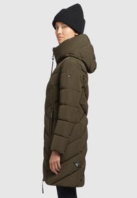 Olijfgroen gewatteerde jas met een hoge kraag, capuchon, een geborduurde design, ritszakken, zijventilen en een merkpatch op de zoom. Dik materiaal en matte afwerking.