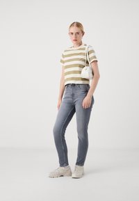 Ριγέ ελαιόχρωμο και λευκό κοντομάνικο μπλουζάκι, στενές ανοιχτό μπλε τζιν, και γκρίζα αθλητικά παπούτσια. Λευκή καμπυλωτή τσάντα φοριέται στον ώμο.