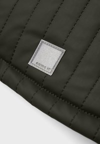 Nahaufnahme von schwarzem gequiltetem Stoff mit vertikalen Nähten und einem kleinen angenähten Quadratlabel mit der Aufschrift "name it" in Kleinbuchstaben.