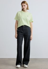 Ανοιχτό πράσινο βαμβακερό κοντομάνικο μπλουζάκι, σε συνδυασμό με ψηλόμεσα μαύρα τζιν παντελόνια με φαρδύ παντελόνι και λευκά αθλητικά παπούτσια. Απλός σχεδιασμός, χωρίς σχέδια.