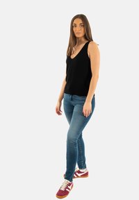 Haut sans manches noir avec un décolleté en V, associé à un jean slim bleu et des baskets bordeaux avec des accents blancs, dotées d'un tissu texturé.