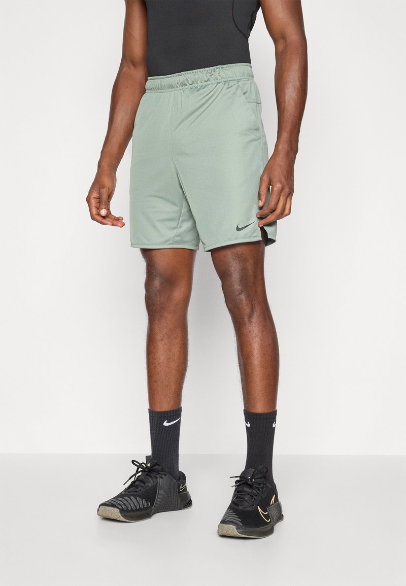 Pantalones cortos deportivos de Nike en verde claro, con una cintura elástica, bolsillos laterales y un logo sutil. Combinados con zapatillas negras y calcetines.