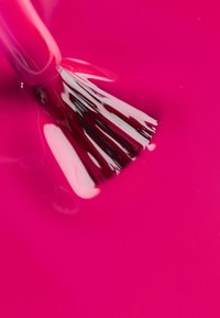 Jasnoróżowy lakier do paznokci o gęstej, błyszczącej konsystencji, z pędzelkiem o czarno-białych włoskach częściowo zanurzonym w lakierze.