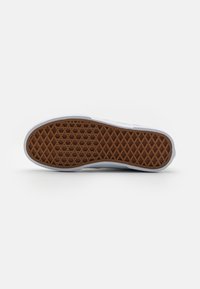 White sneaker sole with a herringbone pattern. Rubber material, featuring textured brown grip and white side accents.