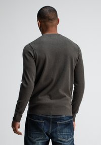 Dunkelgrüner Strickpullover mit langen Ärmeln, Rundhalsausschnitt und gerippten Bündchen, kombiniert mit blauen Jeans aus Denim mit Gesäßtaschen.