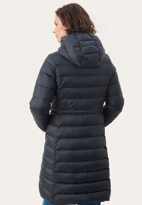 Marineblauwe pufferjas met een gewatteerd ontwerp en capuchon. Middellange lengte, elastische manchetten, zachte textuur, verticale stiksels en gestroomlijnde silhouette.