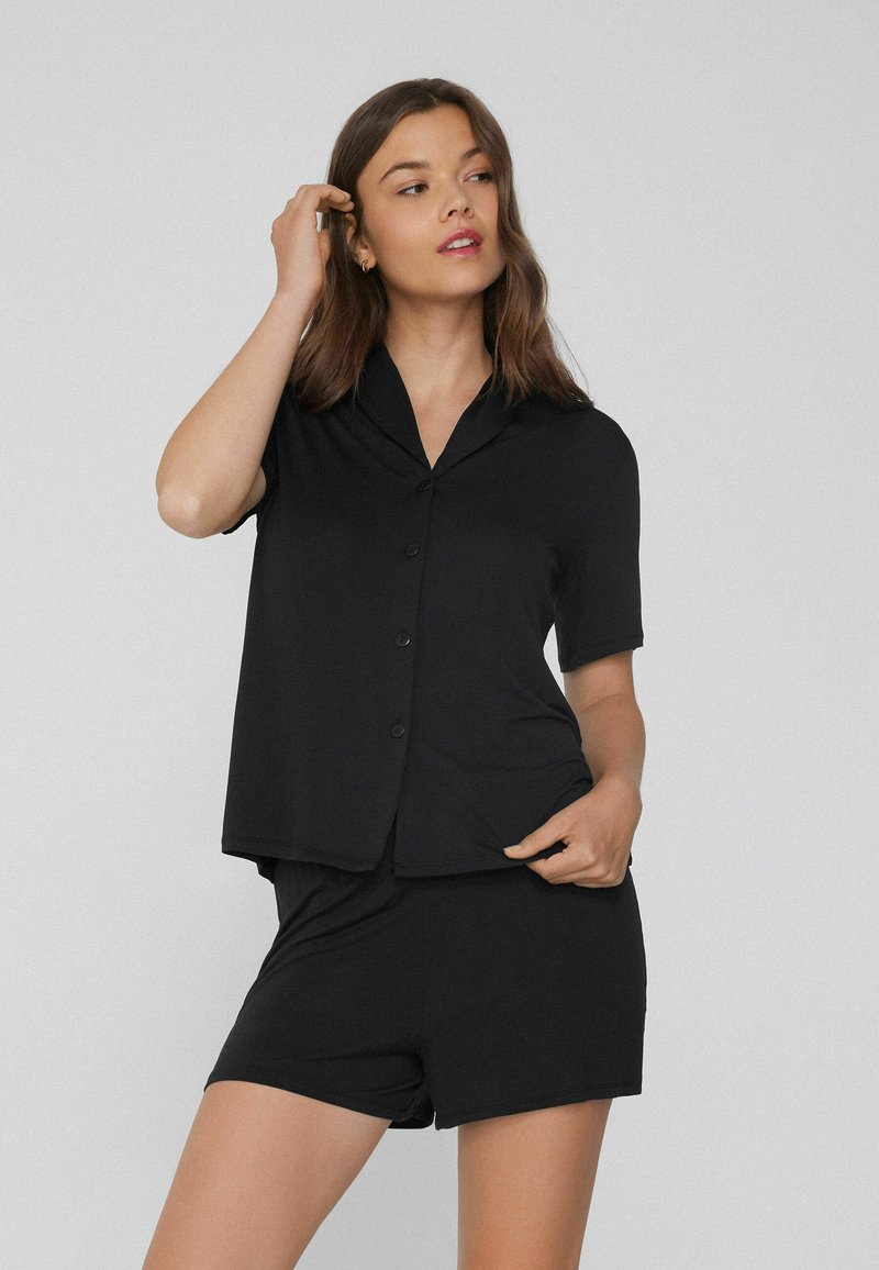Black short-sleeve pajama set featuring a collared button-up top and matching shorts, made of smooth, lightweight fabric.