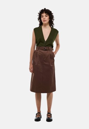 Haut sans manches vert avec un décolleté en V profond et un seul bouton, accompagné d'une jupe marron taille haute avec des plis et une ceinture. Chaussures noires.