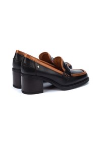 Mocasines de cuero negro con tacón, con un acento marrón alrededor del cuello y un tacón cuadrado grueso. Cuenta con una punta redondeada y detalles de costura.