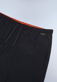 Pantaloni neri con vita elasticizzata, coulisse visibile e fodera interna arancione su sfondo chiaro.
