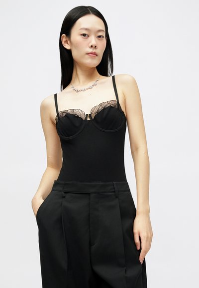 Must must ühine, millel on pitsäärismis kaeluse juures, sisaldab reguleeritavaid rihmu. Komplektis on kõrge vöökoht mustad püksid, luues sujuva silueti.