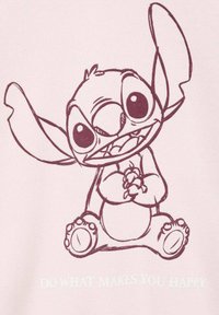 Design di un personaggio di cartone su un tessuto rosa chiaro con contorni rosa scuro, che mostra una creatura aliena sorridente seduta e che tiene le mani, con del testo sottostante.