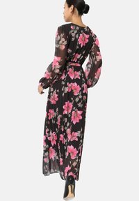 Robe longue noire à motifs floraux, présentant des fleurs roses et blanches, en tissu transparent, à manches longues, avec une taille cintrée et une jupe fluide.